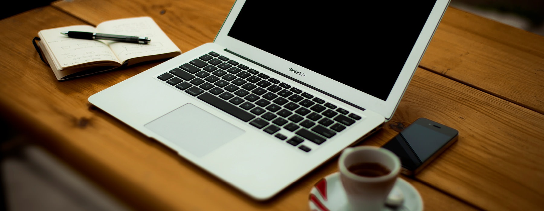 open laptop on desk with notebook and coffee cup